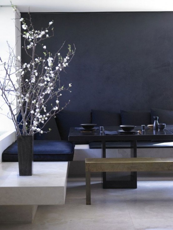 a minimal dining space with a black accent wall, a stone corner bench, blakc upholstery, a black table and a metal bench