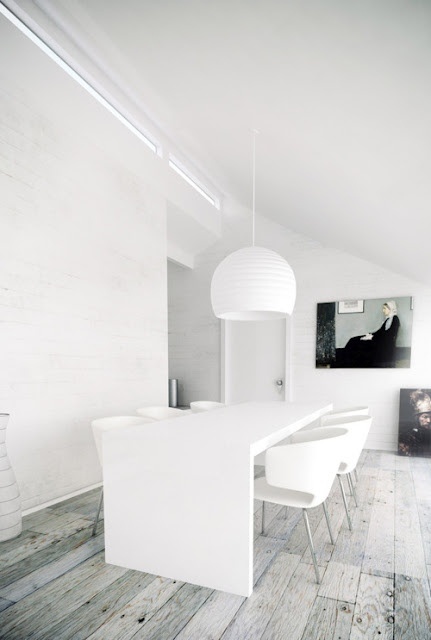 A white minimalist dining space with a large table and chairs, a white pendant lamp is a cool and all minimal space, free of clutter