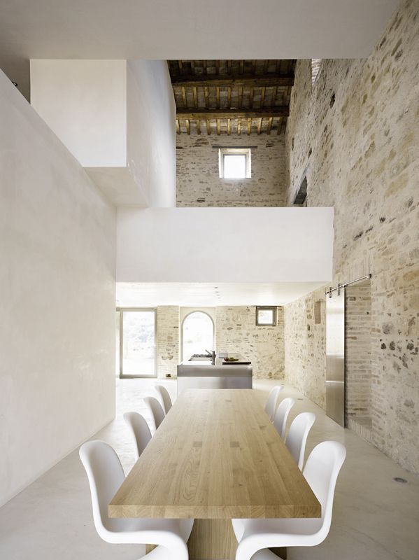 A minimalist dining room with a stone wall and a white one, a light stained table and white chairs is a cool and minimal space to enjoy your meals