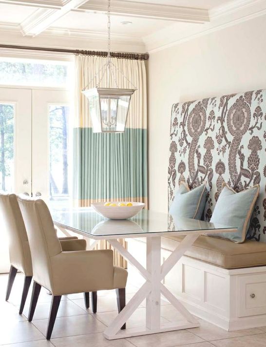 A chic modern dining space with a built in bench with a tall printed back, a glass table, leather chairs and a pendant lamp on chain