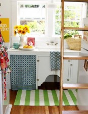a tiny cottage kitchen with white cabinets, printed colorful texitles, a ladder for storing things up and on it