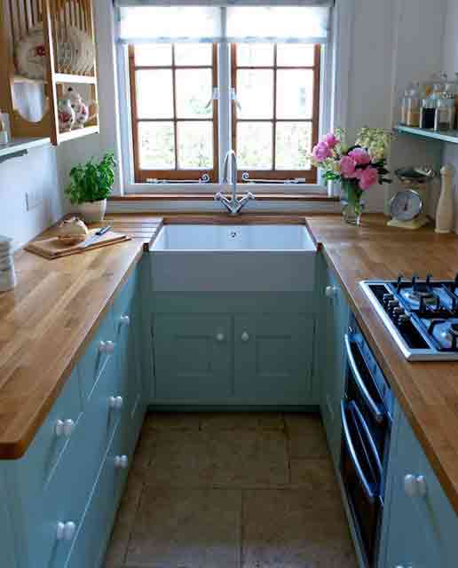 a tiny blue kitchen with butcherblock countertops and open shelves over the cabinets plus a view is cozy and cool