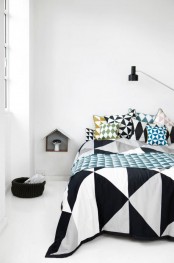a Scandinavian bedroom with a bed with cool geometric bedding, a house-shaped wall-mounted nightstand, a black basket for storage and a table lamp