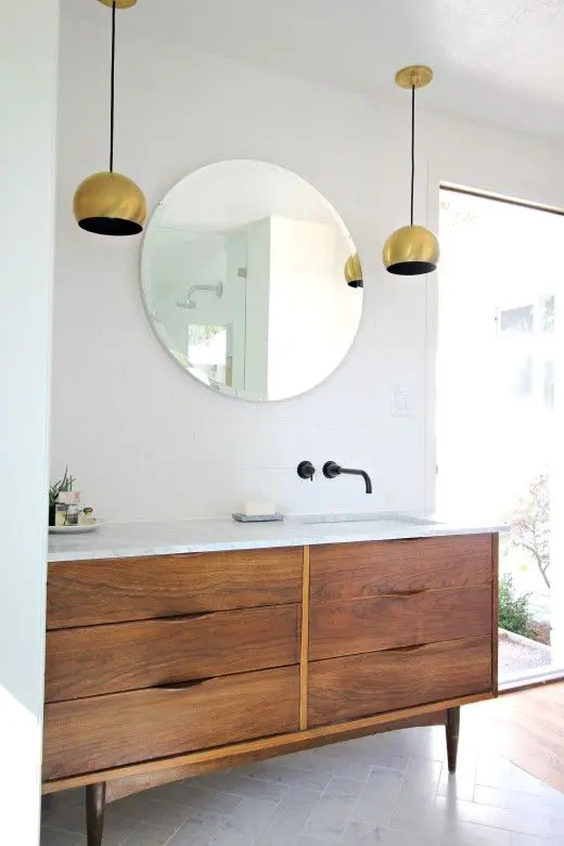 A neutral mid century modern bathroom with white and marble tiles, a wooden vanity, gold pendant lamps and a large floor to ceiling window