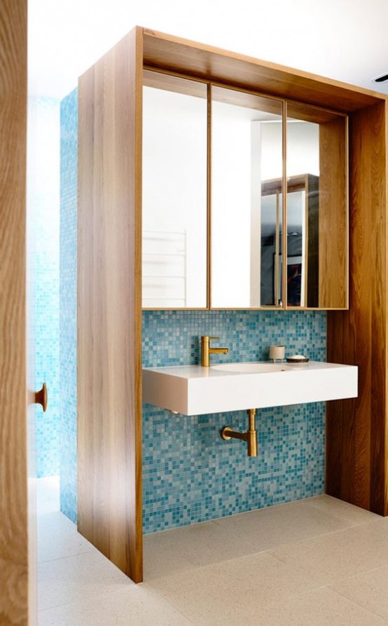 a mid-century modern bathroom with small scale blue tiles and rich stained furniture plus mirrors over the sink is very cool