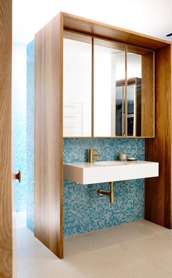 A mid century modern bathroom with small scale blue tiles and rich stained furniture plus mirrors over the sink is very cool
