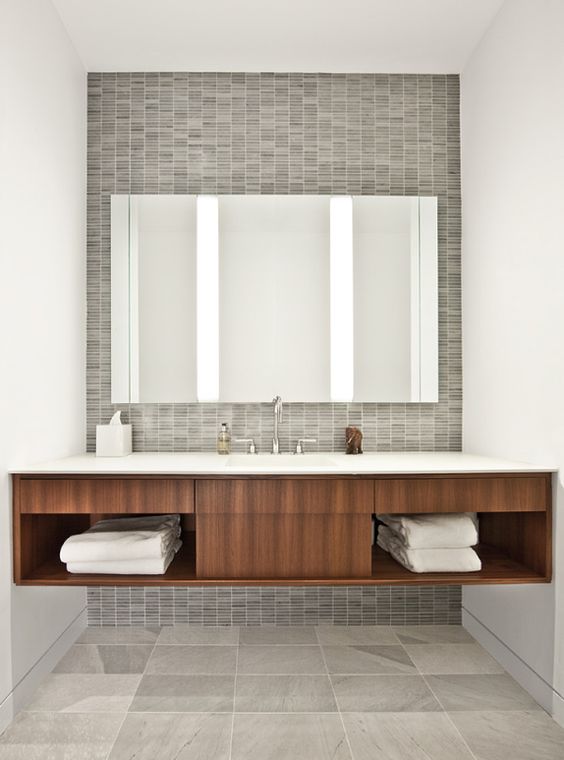 An elegant mid century modern bathroom with grey tiles of various sizes and scales and a large floating vanity plus a statement mirror