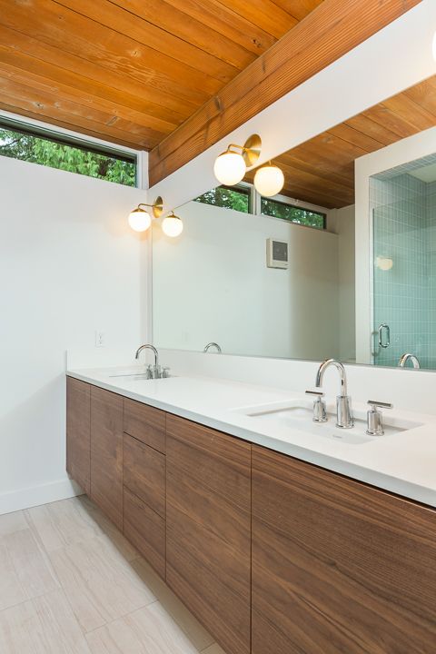 An elegant mid century modern bathroom with a stained wooden ceiling, a stained wooden vanity and all neutrals around plus a narrow skylight