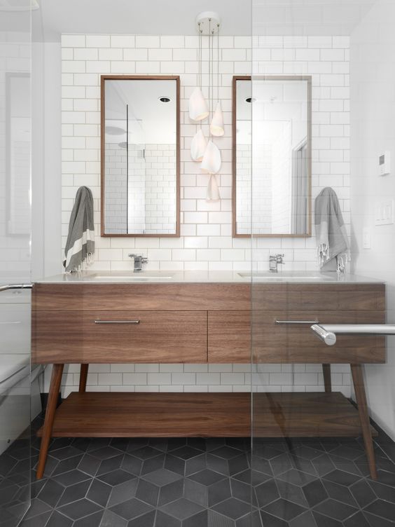 An elegant neutral mid century modern bathroom with subway tiles, a wooden vanity, wooden frame mirrors and catchy geometric tiles on the floor
