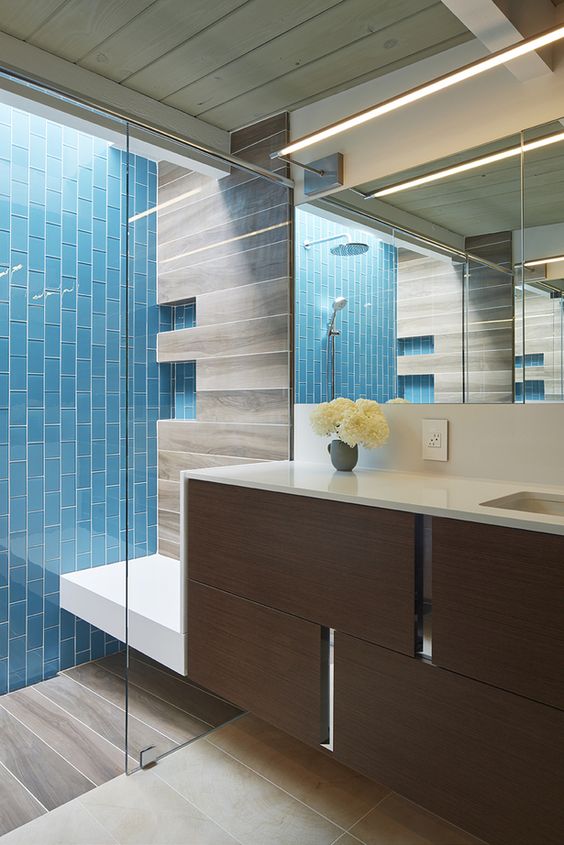 A stylish mid century modern bathroom in neutrals, with a bold blue vertical tile wall, a dark stained floating vanity and a large lit up mirror
