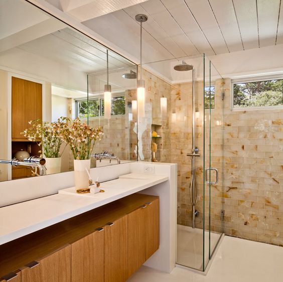 A warming mid century modern bathroom with earthy tiles, a wooden cabinet under the vanity countertop and large mirrors