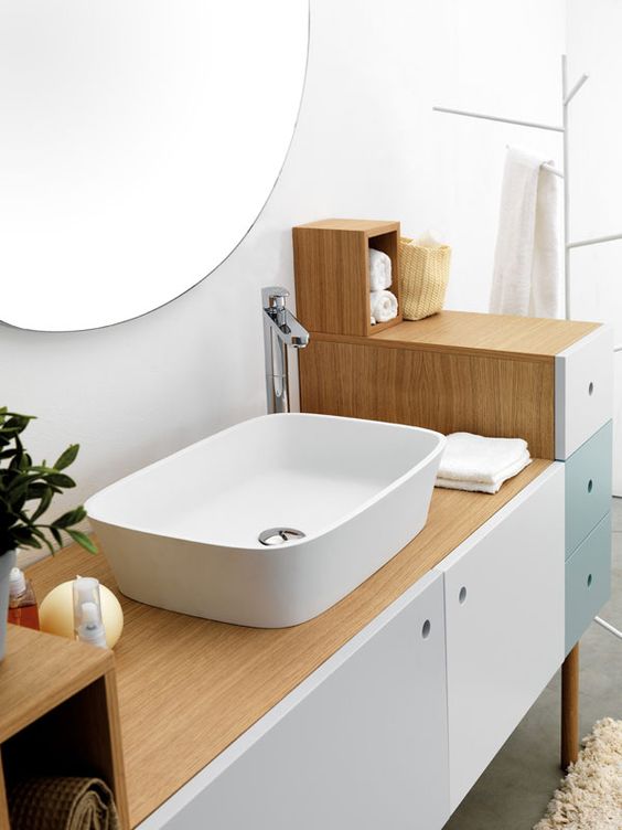 A neutral mid century modern bathroom with a color block vanity, a round mirror and potted greenery