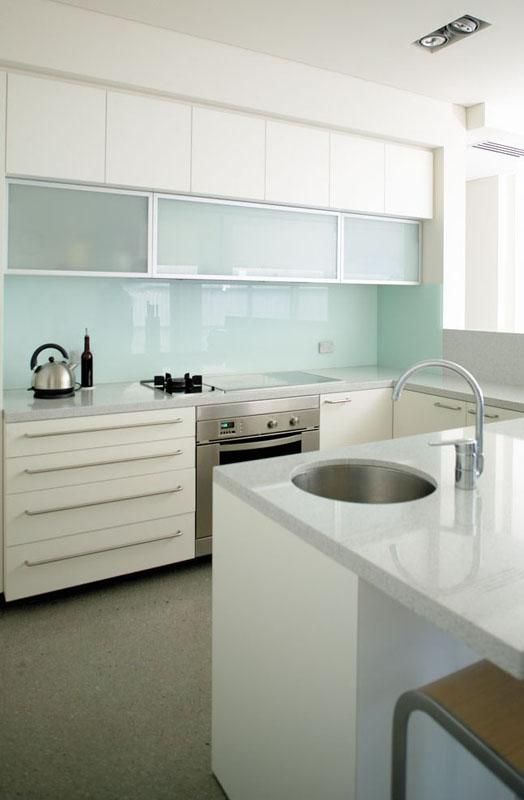 an airy white kitchen with white stone countertops, frosted glass cabinets and a mint glass backsplash is a lovely space