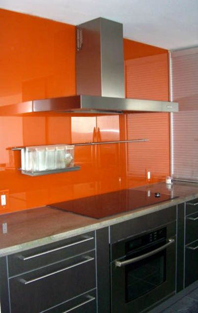 a dramatic black modern kitchen with a bold orange soild glass backsplash for a contrasting touch