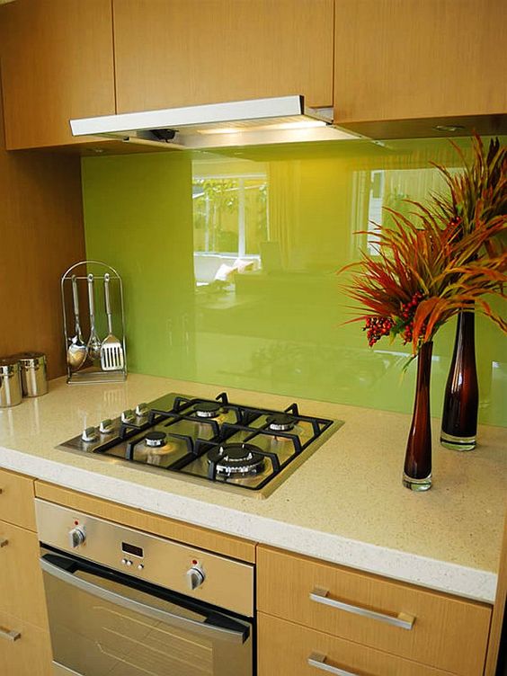 A light stained kitchen with white stone countertops and a neon green solid glass backsplash for a bold and chic touch of color