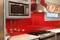 a pale blue kitchen with stainless steel touches, a bold red glass backsplash and a bold floral curtain for a touch of color
