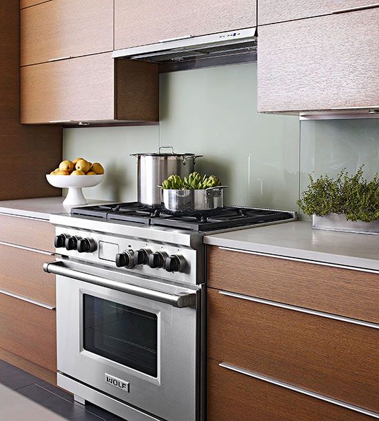 A rich stained modern kitchen with stainless steel touches, white stone countertops and a light grene solid glass backsplash for a sleek touch