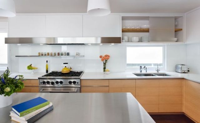 A modern light stained kitchen with white stone countertops and a glossy white glass backsplash is a chic space with much style
