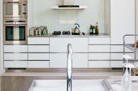 a modern white kitchen with stainless steel touches and a white solid glass backsplash to add a glossy touch to the room