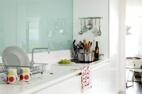 a minimalist white kitchen with white stone countertops and a mint glass backsplash is a stylish and catchy space in soft shades
