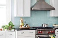 a modern white kitchen with shaker cabinets, black stone countertops and a blue glass backsplash for a dainty touch of color