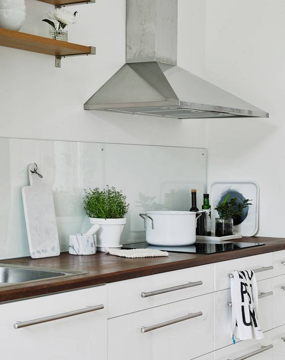 A white Scandinavian kitchen with dark stained butcherblock countertops and a clear glass backsplash that helps to create a calm feel