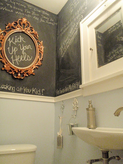 A catchy powder room with color block walls, half light blue, half chalkboard, with a wall mounted sink and a toilet, is a cool and lovely space