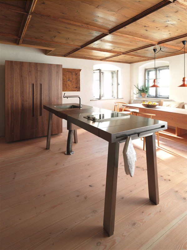 A contemporary wood and metal kitchen island designed as a table to look more lightweight, with a sink and some holders