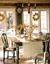 a vintage rustic Thanksgiving tablescape done with a burlap runner, wheat in vases and a tray with nuts, acorns and large candles as a centerpiece