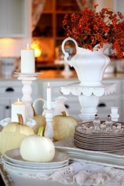 beautiful vintage Thanksgiving tablescape with neutral pumpkins, white porcelain, white candles and dried flowers in a jug, vintage plates