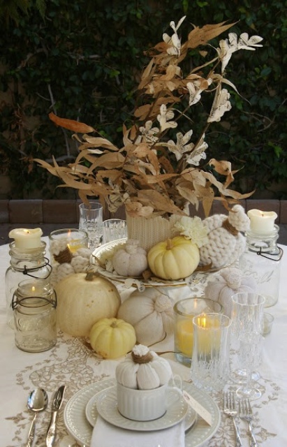 a vintage rustic Thanksgiving tablescape with a lace runner, white textiles, a dried leaf and flower centerpiece, white and neutral pumpkins, candles in glasses and white porcelain is a chic one