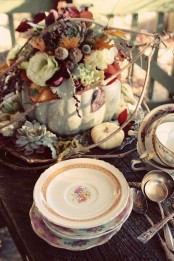 a vintage rustic Thanksgiving tablescape done with a farmhouse centerpiece – a pumpkin with blooms, leaves and berries and vintage porcelain and cutlery