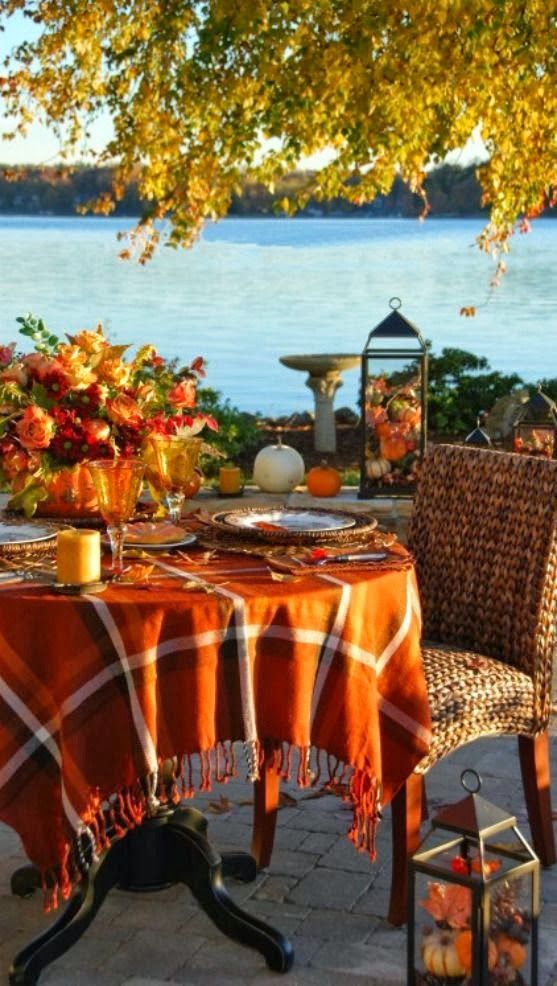 A Thanksgiving tablescape with a bright plaid tablecloth, a bold fall colored floral centerpiece, amber glasses and a cool view