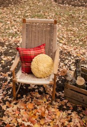 a wicker chair with a duo of pillows – a neutral round pillow and a red plaid pillow is a cool solution for a fall or Thanksgiving porch