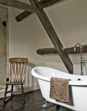 a modern farmhouse bathroom with neutral walls, a wooden floor and matching wooden beams plus a vintage bathtub