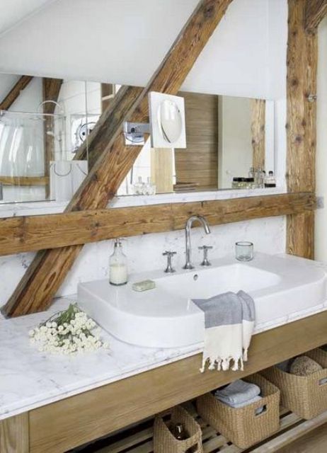 a farmhouse bathroom in white, with wooden beams and a wooden vanity, a white sink and a long mirror