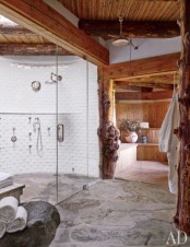 an eclectic bathroom with a stone floor, a shower clad with white tiles, a skylight, a sauna space and wooden beams on the ceiling