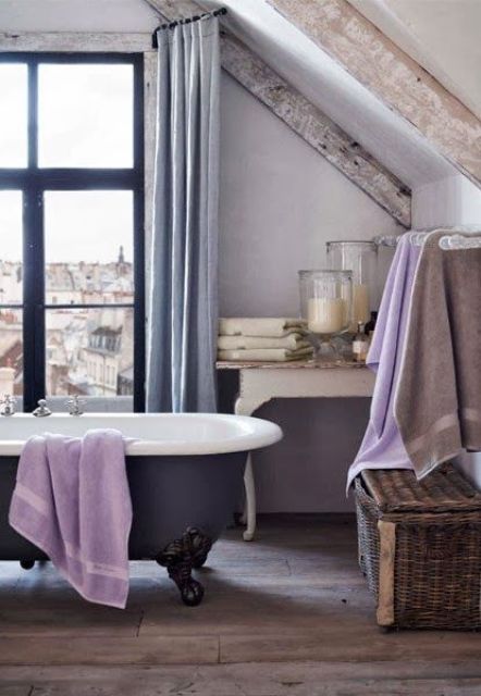 A vintage inspired bathroom in neutrals and pastels, with a refined tub, lilac textiles, grey curtains and whitewashed wooden beams for a worn look