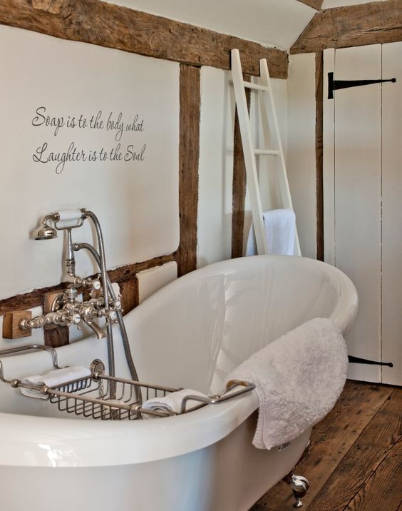 A refined vintage inspired bathroom in white, with a wooden floor, wooden beams and a chic tub plus vintage fixtures