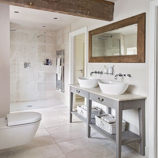 a modern rustic bathroom with neutral tiles, a vanity with two sinks, a wood frame mirror and wooden beams