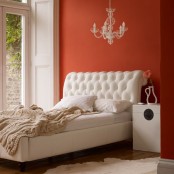 an orange bedroom with a creamy bed and neutral bedding, a chic chandelier and a chest-like nightstand