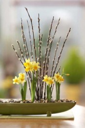 a spring centerpiece of a wooden bowl with pebbles and yellow daffodils plus willow is a cool spring decoration