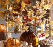 a fall branches with leaves arrangement in a large amber vase plus some faux pumpkins around is a timeless idea for seasonal home decor