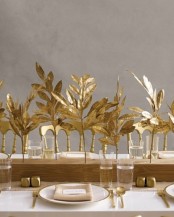 a centerpiece of a wooden slab with gold leaves inserted match the gold cutlery and spruce up the fall tablescape