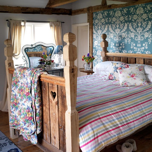 a bright bedroom with floral bedding, a striped blanket, a statement wall and a carved wooden bed feels like rustic spring
