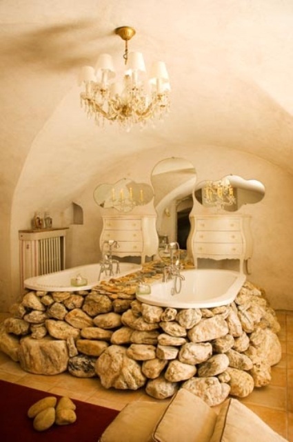 A unique cave like bathroom with a crystal chandelier, vintage dressers and a couple of bathtubs clad with real stones