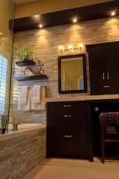 a modern bathroom done with decorative stone and dark furniture plus lights for a contrasting and bold look