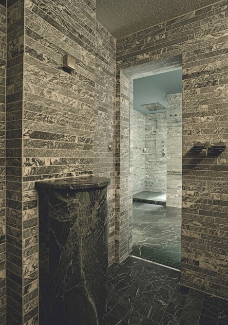A minimalist bathroom fully clad with tiles that imitate real stone and a stone fre standing sink