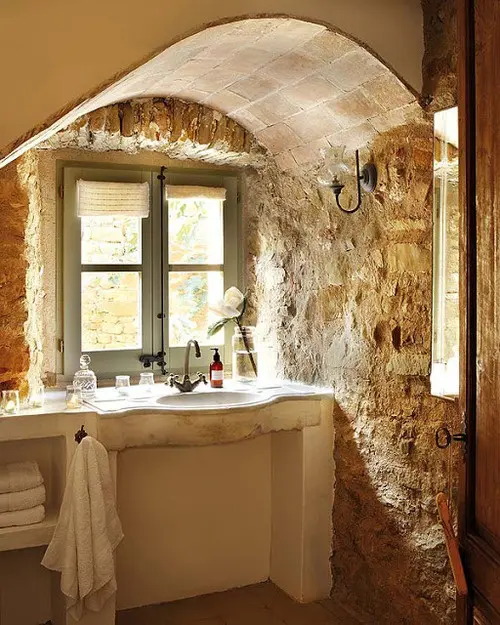 Walls of real rough stone are highlighted with an arched stone ceiling and a neutral vanity built in