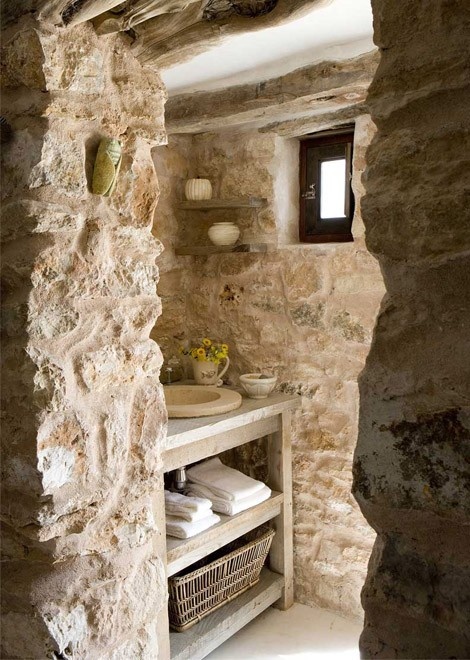 a farmhouse bathroom fully clad with real stone and with a wooden vanity plus floating shelves